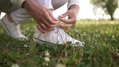 戴着结婚戒指的女<strong>跑步</strong>者的双手在绿色草地上的白色<strong>运动鞋</strong>上系紧鞋带